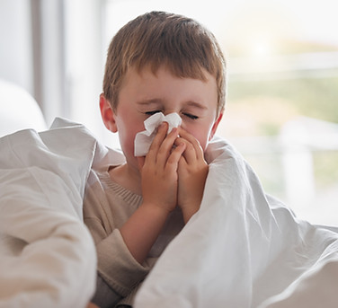 My nose wont stop dripping. Shot of a little boy feeling ill in bed at home and blowing hi