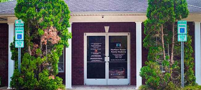 The outside of the brown brick Northern Rowan Family Medicine building with a gray roof and greenery flanking both sides of the door.