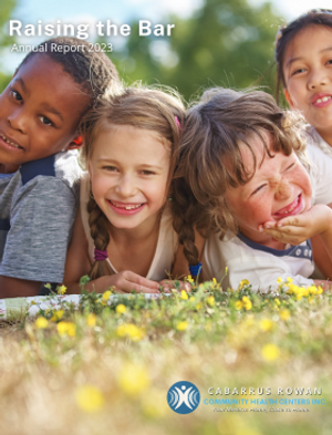 Front cover of 2023 CRCHC Annual Report, showing four young children smiling while laying down on grass with yellow flowers.