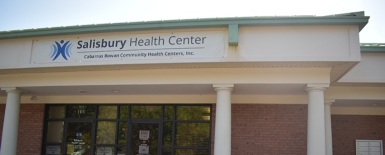 The front enterance of the red brick and white plaster Salisbury Health Center with the CRCHC logo on top of the door and on the door.
