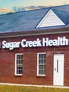 Exterior of red brick building with large white lettering spelling out Sugar Creek Health Center.