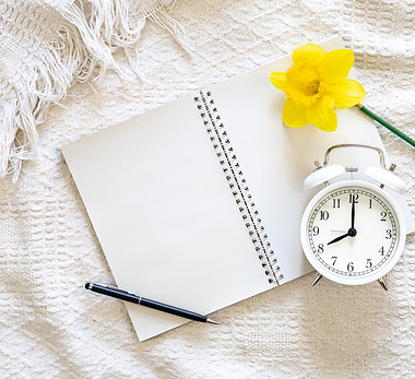 open-blank-notebook-yellow-flower-white-alarm-clock-white-bed-top-view.jpg