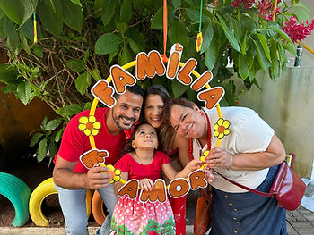 família composta por três adultos e uma criança posando por trás de um círculo florido com a frase "Família é Amor" em exposição