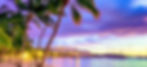 "Scenic tropical resort at sunset with palm trees, calm ocean water, and colorful sky."