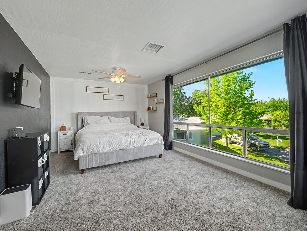 Spacious bedroom with a large picture window overlooking a landscaped residential property.
