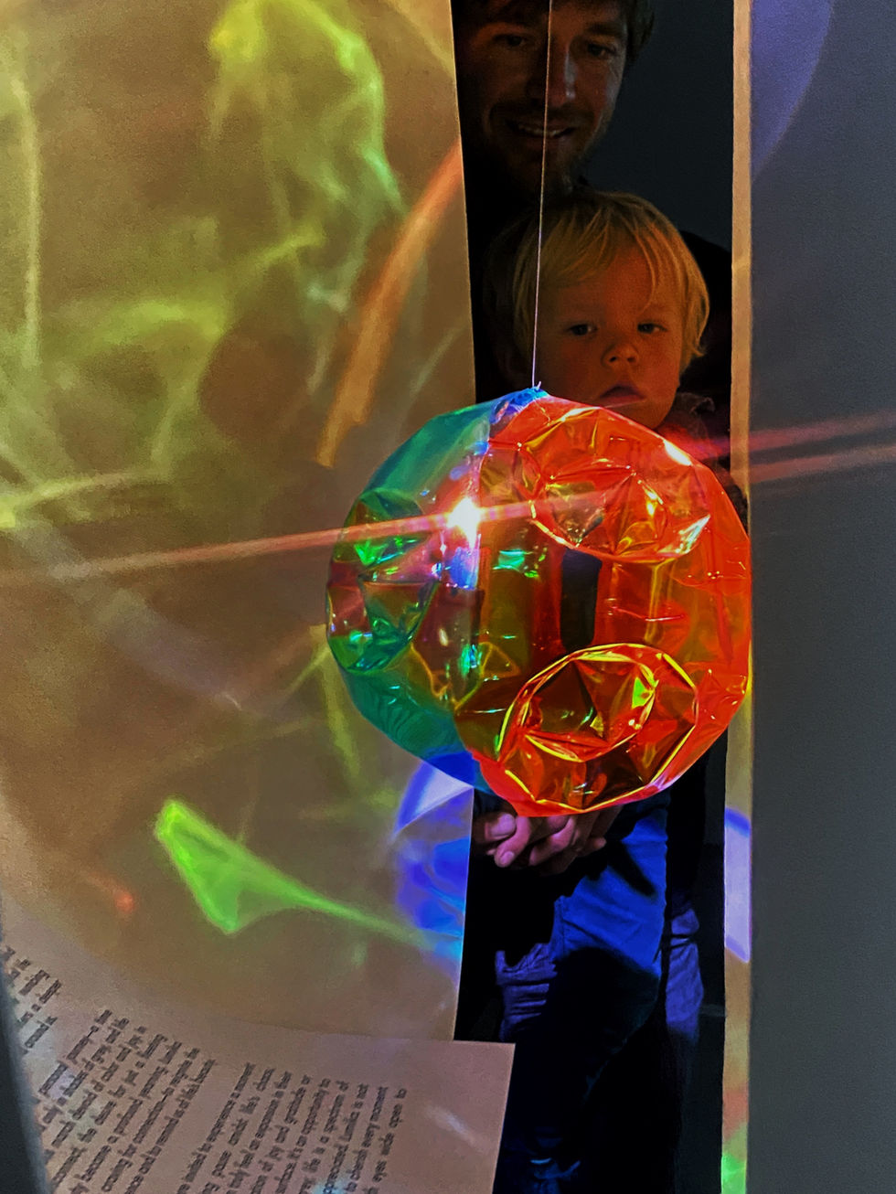 A child taking a glimpse into the reflection of multiple colors in organic rays of light of dichroic sculpture installation.