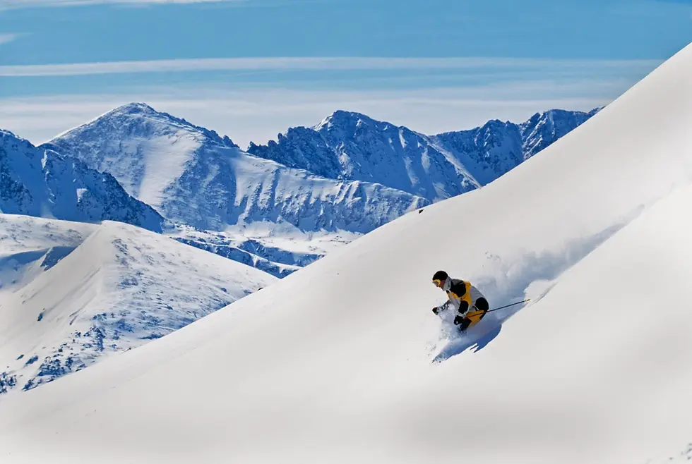 Skier skying down snowy mountain ridge above a high-altitude ski resort at sunrise