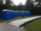 Row of blue portable toilets near a wooden ramp.