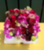 A vibrant bouquet of red and pink roses sits on a yellow table against a dark green background, creating a cheerful, colorful display.