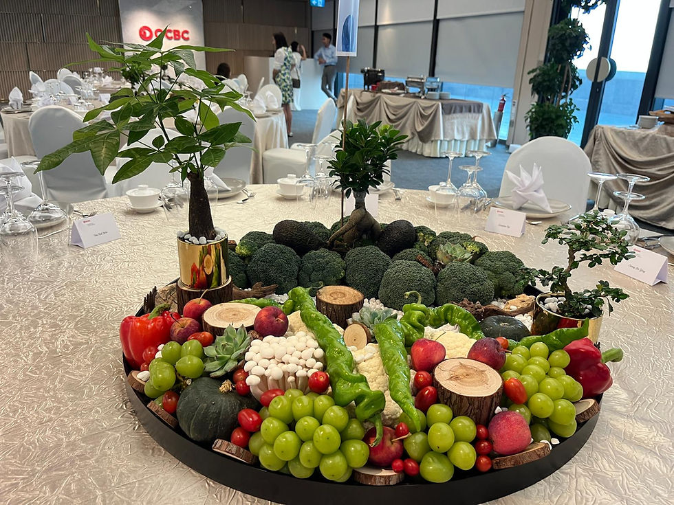 Elegant banquet table with a centerpiece of assorted fruits, vegetables, and plants. White tablecloths and place settings. OCBC logo visible.