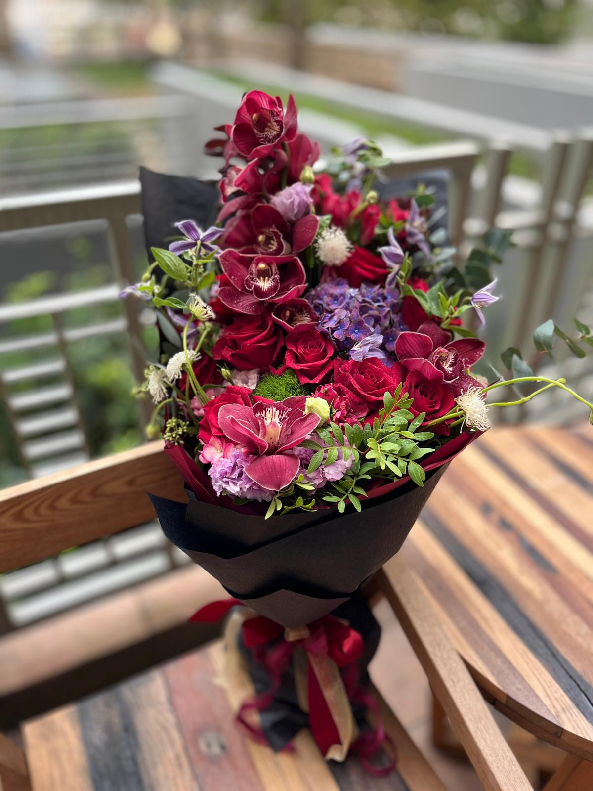 A vibrant bouquet of flowers arranged in a green paper bag, showcasing a variety of colors and textures.