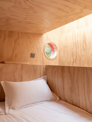 红色潜水艇小屋:阁楼床位旁的圆形舷窗,把树影收进卧室。
Red Submarine Cabin: A porthole beside the loft bed draws the trees close to the sleeping area.