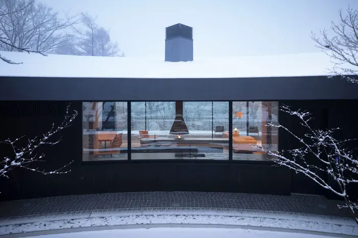 THE CONE轻井泽共享别墅 冬季从北侧水庭看建筑 屋面与暖色室内在积雪和林木之间形成对照
THE CONE shared villa in Karuizawa, Across the winter water garden, the roof and warm interior stand against snow and bare woodland