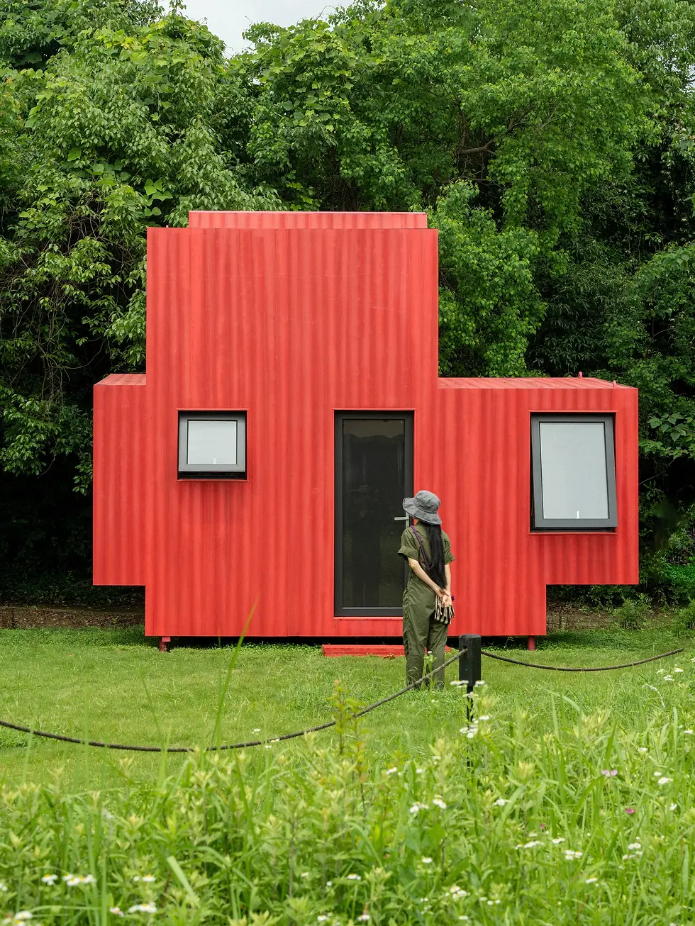 红色潜水艇小屋:从草地看侧立面,架空的小屋轻轻离开地面。
Red Submarine Cabin: From the lawn, the raised side elevation shows how the cabin meets the ground.