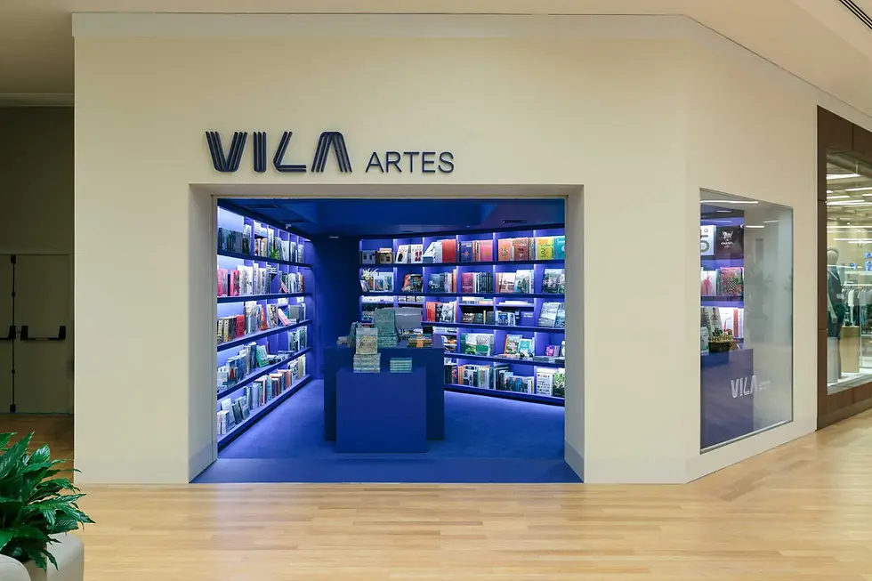 Livraria da Vila Artes,米白色店面从商场木地板旁切出深蓝入口,书架与中央展台在门框中形成完整的第一眼。
Livraria da Vila Artes, An off-white storefront cuts a deep-blue opening beside the mall's timber floor, framing shelves and the central display in a single first view.