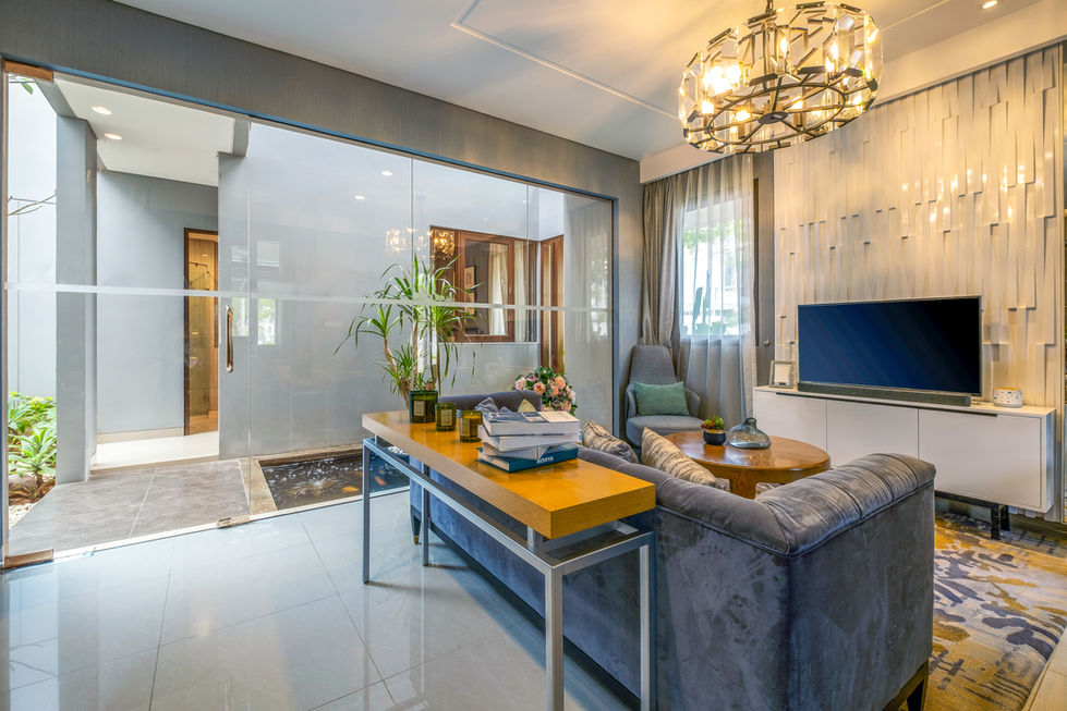 Modern living room featuring a grey sofa, decorative TV feature wall, and glass walls overlooking an indoor koi pond.
