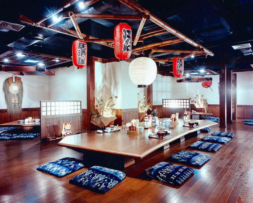 Traditional Japanese low-table dining room featuring blue floor cushions and red paper lanterns hanging from a bamboo ceiling structure.