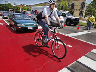 A cyclist rides on a red-painted street ahead of cars.