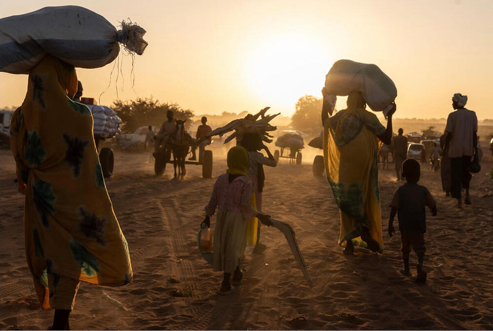 Adults and children walk away from the camera, backlit by the sun, carrying belongings on their heads.
