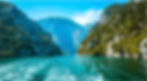 Serene blue-green waterway framed by rising rocky slopes with trees.