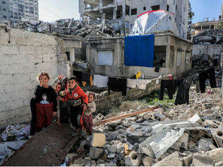 Image of buildings in ruins, some still partially standing. 5 young. children are standing in the rubble, posing for the picture.