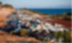 Piles of waste along a dirt road, with blue sea and mountains in the distance.