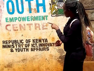 A woman points at a large sign on a building that says: Muchatha Youth Empowerment Centre, Republic of Kenya Ministry of ICT, Innovation & Youth Affairs.