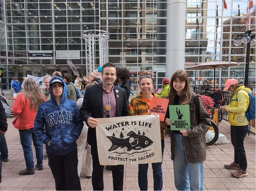 Photo of three youth and an adult holding signs. The central sign reads "Water is Life. Protect the Sacred". 