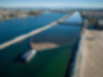 An aerial view of a river being cleaned by an Interceptor boat. The boat is attached to a U-shaped net that is collecting trash.