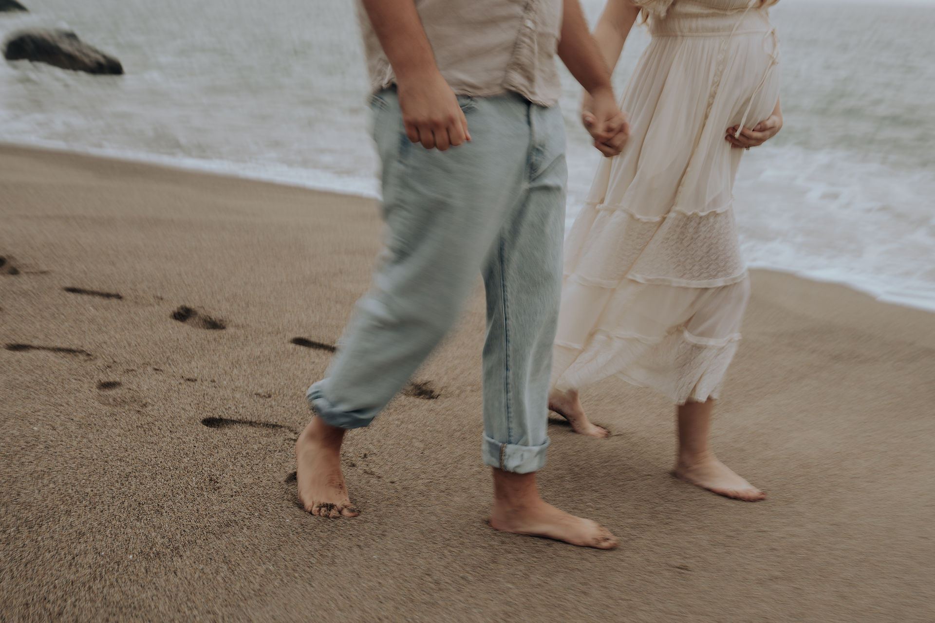 Barefoot couple walking along the shoreline during a cinematic maternity session in Malibu.