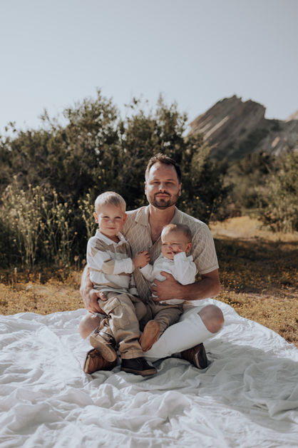 A father cradles his two young sons in his lap, creating a tender and heartwarming family moment against the backdrop of Vasquez Rocks. Santa Clarita family photography with an emphasis on emotions.