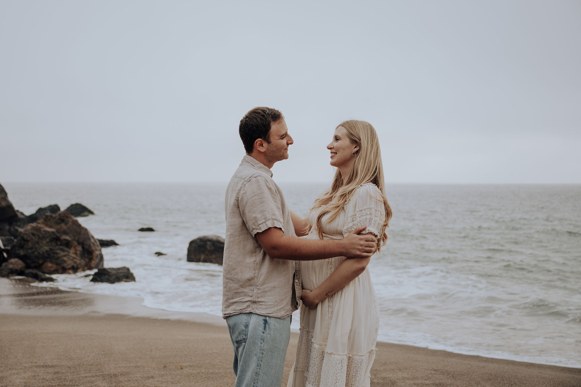 Romantic maternity session at Point Dume beach with an expecting couple standing by the shoreline.