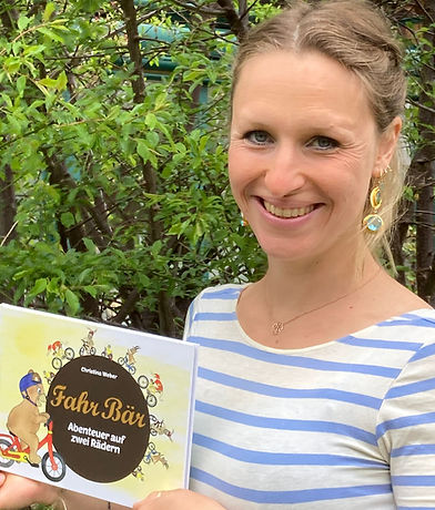 Christina Weber, die Buch-Autorin, in einem weiß-blauen Shirt, mit ihrem Buch, vor einem Baum
