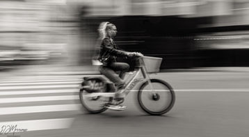 Bicyclist riding along Rue de Rivoli in Paris, captured with a shutter drag effect creating motion blur, with historic architecture visible in the background.