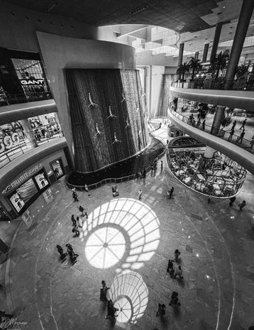Indoor waterfall wall at Dubai Mall featuring cascading water over sculpted divers, with natural light filtering through and shoppers visible in the background.