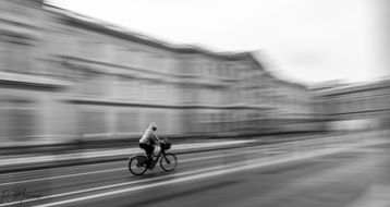 Bicyclist riding along Rue de Rivoli in Paris, captured with a shutter drag effect creating motion blur, with historic architecture visible in the background.