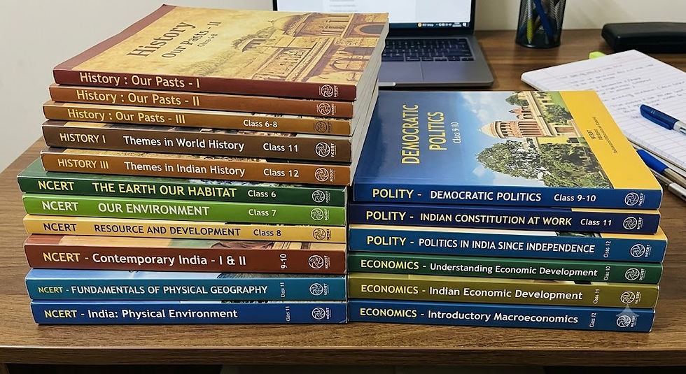 Two stacks of NCERT textbooks for UPSC preparation neatly arranged on a wooden study desk, with a laptop, open notebook, and pens in the background. The left stack contains History and Geography books from Classes 6 to 11, and the right stack features Polity and Economics textbooks from Classes 9 to 12.