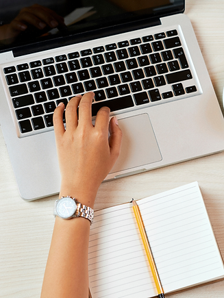 Typing on a laptop with a notebook and coffee nearby