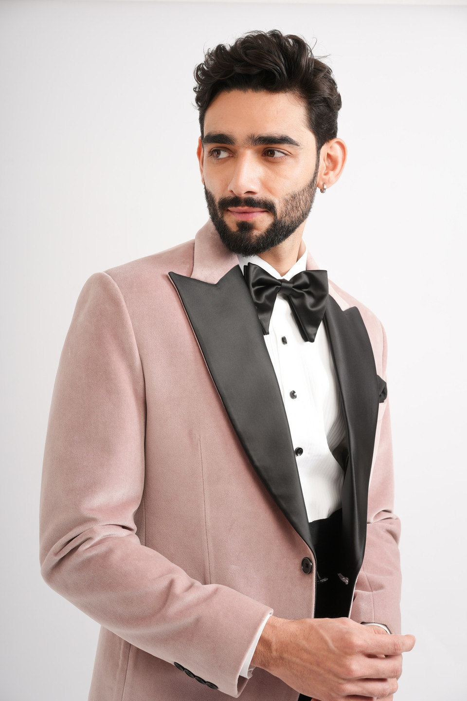 Close-up of a light pink velvet tuxedo jacket featuring a black satin shawl lapel and elegant formal tailoring.