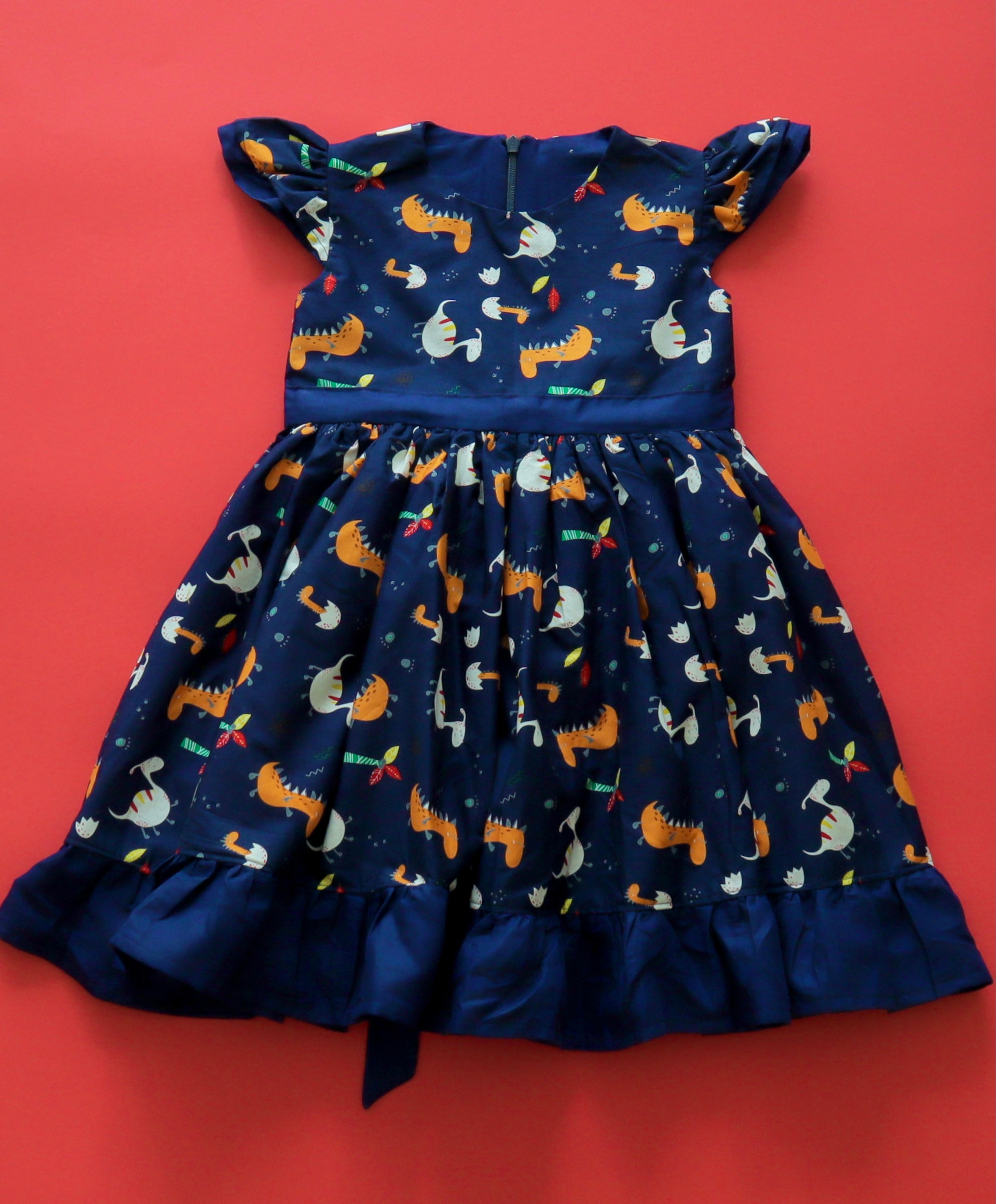 navy blue dinosaur fabric. It has an invisible zipper at the center back and it’s fully lined, with a ruffle at the bottom e