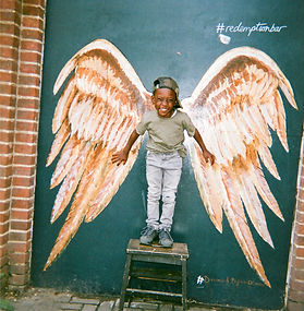 Boy standing on stool in front of a mural with angel wings.