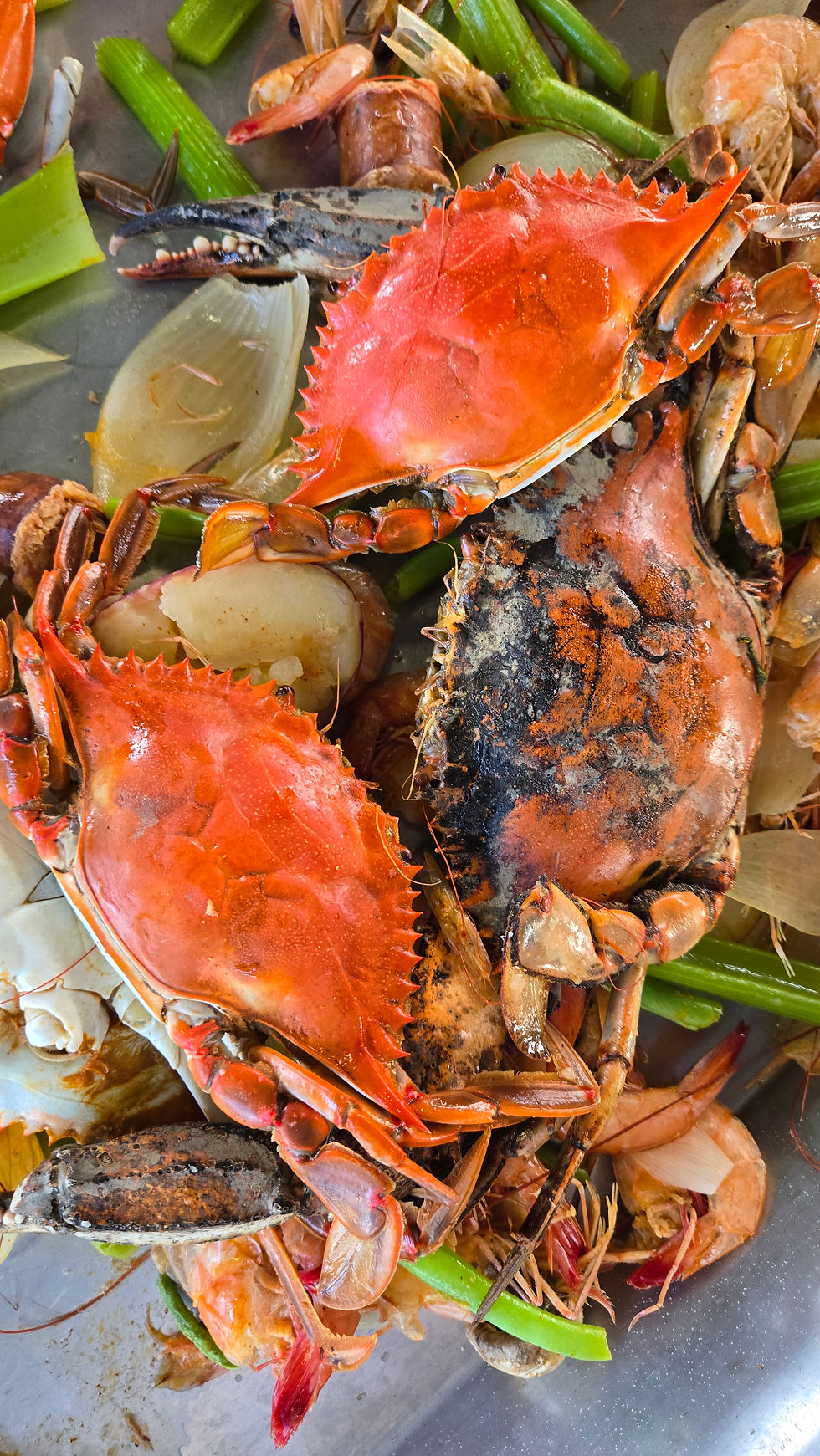 Close-up of cooked bright red crabs and shrimp with green vegetables on a metal tray, a hearty seafood feast.