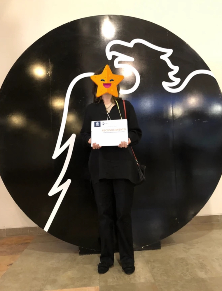 Me standing before my university's shield with my master's diploma 