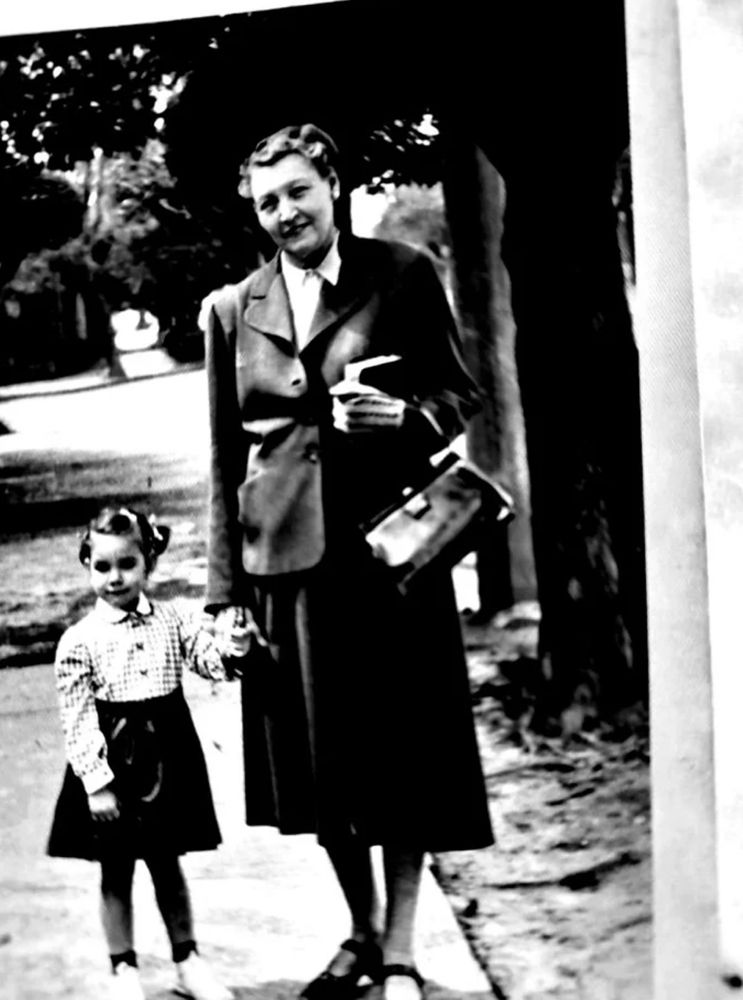 A woman and a small child stant on a street surrounded by trees