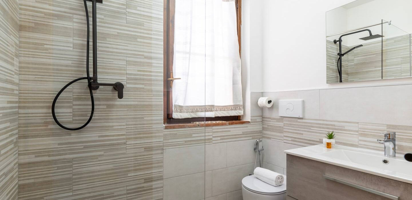 Interno bagno moderno con doccia, WC, lavabo, specchio e finestra.