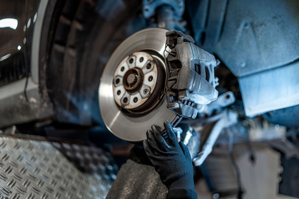 Mechanic with black gloves working on a car brake disc in a garage. The setting has a metallic, industrial backdrop.