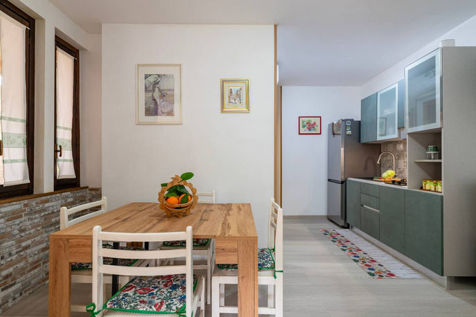 Sala da pranzo luminosa con tavolo in legno e cucina moderna attrezzata.