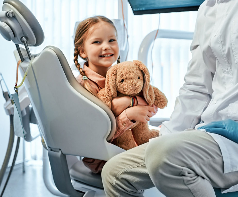 Bambina sorridente sulla poltrona dentistica con peluche.