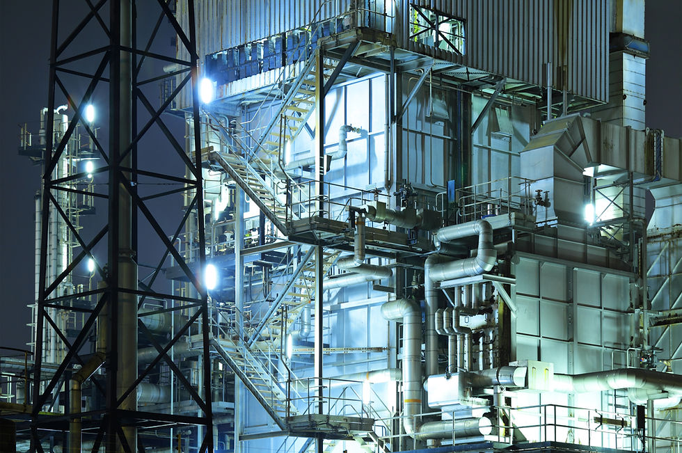 Industrial complex illuminated at night with metal structures, pipes and bright lights.