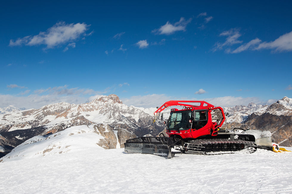 Red snowcat on snowy slope, mountain peaks under blue sky.
